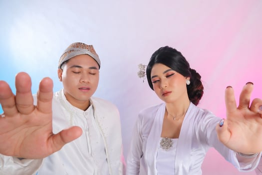 A pair of indonesia men and women with their eyes closed, hands facing forward, wearing modern Javanese traditional clothing, white velvet bridal kebaya, wedding concept with a white studio background photo