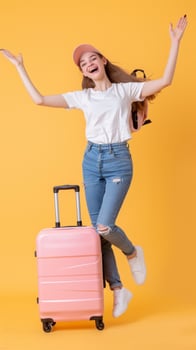 Excited Young Woman Jumps With Pink Suitcase on Yellow Background photo