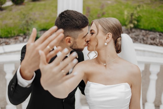 A bride and groom kiss each other's hands in a wedding photo. The bride is wearing a white dress and the groom is wearing a suit photo