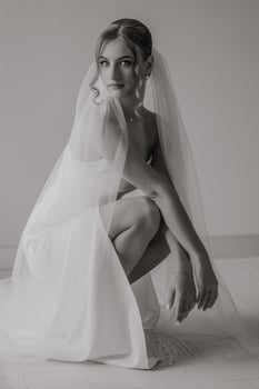 A woman in a white dress is posing for a photo with a veil. She is wearing a ring and a necklace