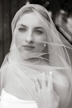 A woman is wearing a veil and has her hand on her hip. She is wearing a white dress and has a ring on her finger photo