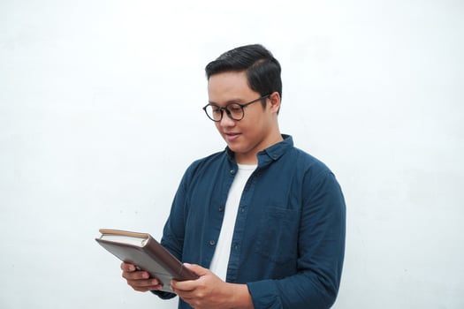 Young Asian man holding a book while thinking and concentrating. Asian student looking for ideas while studying over white background photo