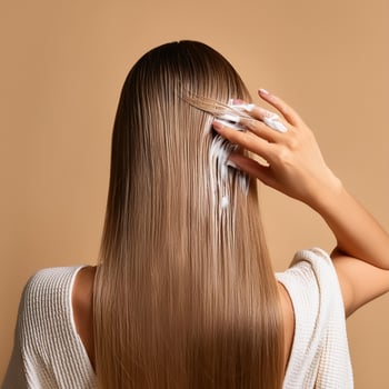 Young woman applying hair mask on beige background, back view photo