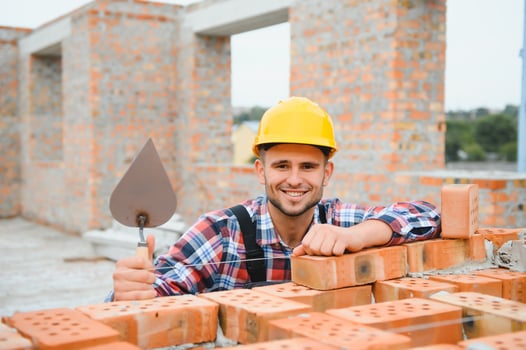 Using bricks. Young construction worker in uniform is busy at the unfinished building photo