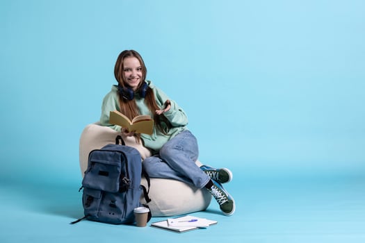 Portrait of cheerful young girl reading book, enjoying hobby, being entertained, studio background. Upbeat woman with novel in arms relaxing, having fun with interesting story photo