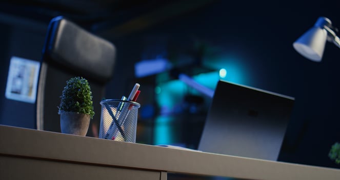 Office desk filled with productivity items in empty home interior illuminated with neon lights at night. Laptop on table and other work related objects in apartment room, camera B close up shot photo