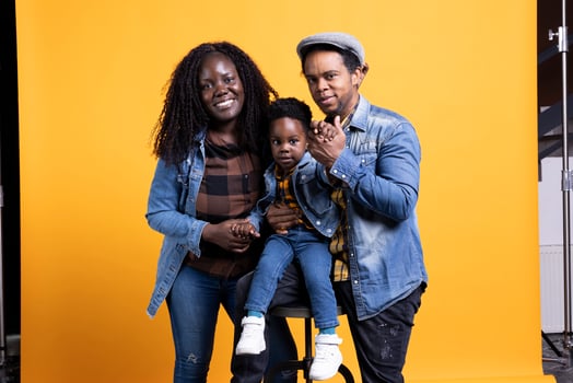 African american joyful family posing together against yellow background, happy couple hugging their little toddler. Smiling young mother and father showing affection to their kid on camera. photo