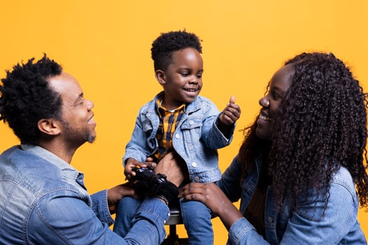 African american parents enjoying time with their baby boy, laughing and embracing him against yellow background. Young happy mother and father bonding with their child in studio. photo