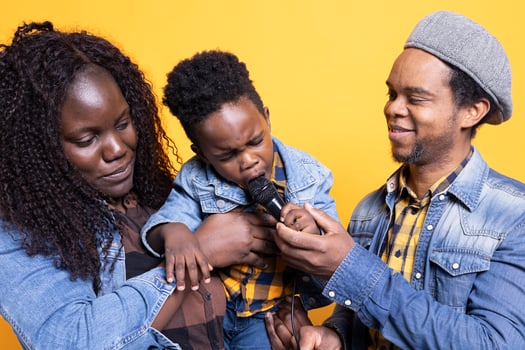 African american couple teaching their small kid how to sing on microphone, learning to perform melody from a young age. Cute little child singing a new song in front of the camera. photo