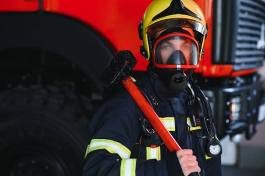 Photo of young fireman with sledgehammer in hands near fire engine