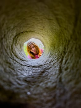 A young girl peers down a hole in granite, her face framed by the rugged stone. Her curious expression and the unique perspective create an engaging and playful scene, perfect for illustrating curiosity, exploration, and childhood adventures. photo
