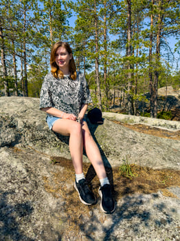 A young woman sitting on a rock in a pine forest under a clear blue sky, enjoying the serenity of nature. Perfect for themes of outdoor adventure, relaxation, and nature appreciation photo