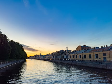 A tranquil scene of a canal in St. Petersburg, Russia, captured at sunset. The calm water reflects the colorful sky, while historic buildings line the canal, creating a picturesque and peaceful evening view photo