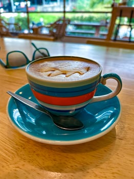 A close-up of a creamy cappuccino served in a vibrant striped cup with a matching saucer and spoon, set on a wooden table in a cozy cafe, with sunglasses and a scenic view in the background photo