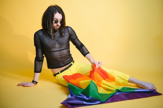 Gay man wearing bright pink top hold rainbow striped flag isolated on colored background studio portrait. People lifestyle fashion lgbtq concept photo