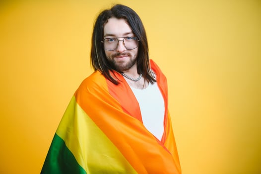 Handsome young man with pride movement LGBT Rainbow flag on shoulder against white background. Man with a gay pride flag. photo
