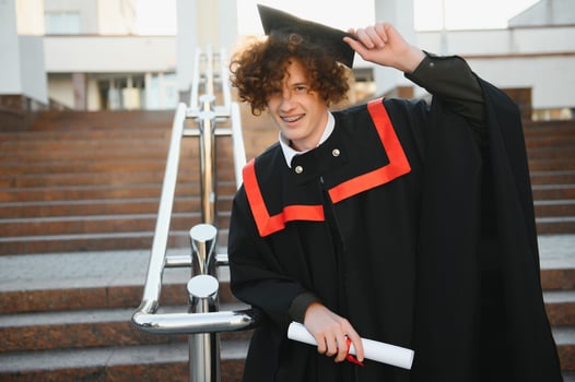 excited graduate student in gown with risen hands holding diploma. photo