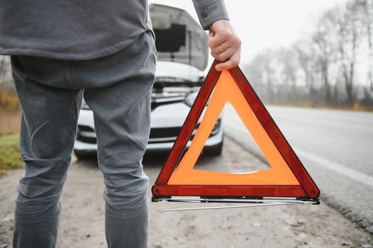 A young man near a broken car with an open hood on the roadside. photo