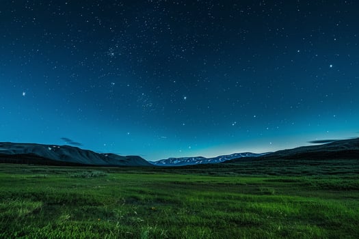 the night sky over a grassy field with mountains in the background photo