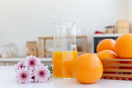 Fresh orange fruit, pink chrysanthemum flower and orange juice in jug on counter at home kitchen. Sweet and tasty fruit with blurred background home kitchen. photo