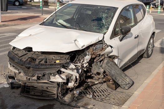 Severely damaged white car after an accident, showcasing the shattered windshield and crumpled body. Ideal for use in materials related to vehicle safety, insurance, and accident awareness campaigns. photo