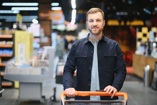 Customer In Supermarket. Man Doing Grocery Shopping Standing With Cart Choosing Food Product Indoors. African American Guy Buying Groceries In Food Store. Selective Focus, Copy Space. photo