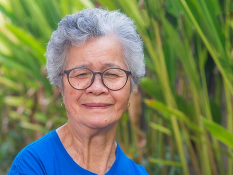 Portrait of a beautiful senior woman with short gray hair wearing glasses, smiling with arms crossed, and looking at the camera while standing in a garden. Concept of aged people and healthcare photo