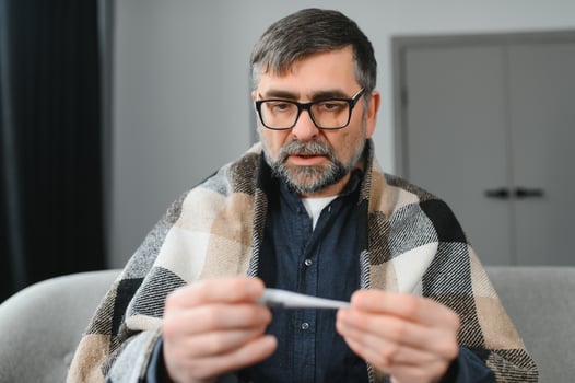 Portrait of sick senior man with thermometer posing at home photo