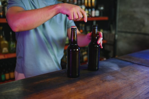 Barman bottle of beer. Nearby empty glass on wooden bar counter in interior of pub, cropped, free space. photo