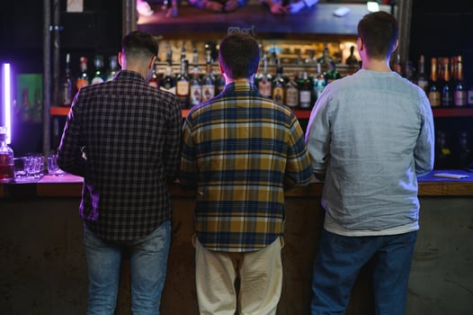 Three young men in casual clothes are smiling, holding bottles of beer while standing near bar counter in pub photo