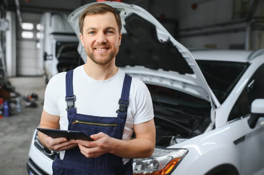 Bearded mechanic in overalls standing in garage of a car salon and holding tablet. He is about to diagnostic breakdown. photo