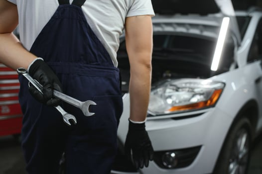 With tool in hand. Adult man in colored uniform works in the automobile salon photo