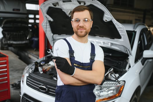 With tool in hand. Adult man in colored uniform works in the automobile salon photo
