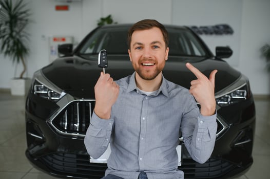 Emotional handsome guy raising hand up and smiling at camera. Rich man buying auto at luxury dealership salon photo