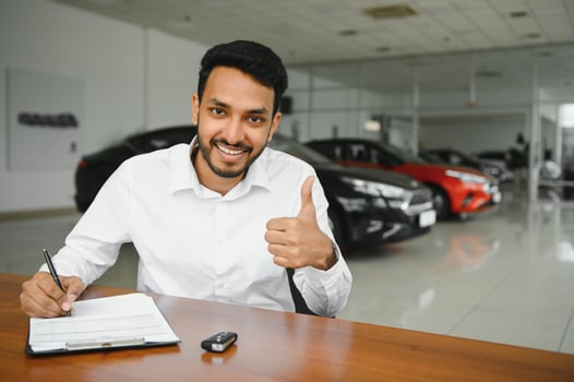 young indian man signing documents at car dealership photo