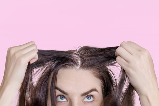 Caucasian brunette woman shows grown gray hair. Isolated on pink background. Close up photo