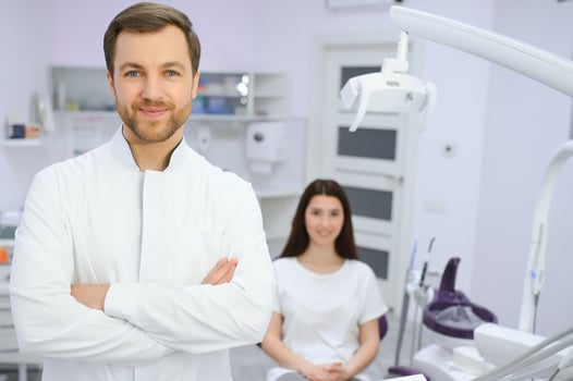 Portrait of positive male dentist with crossed hands posing at camera with patient and nurse on background photo