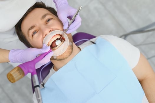 Periodontal Services. Closeup Shot Of Smiling Man Getting Treatment In Stomatologic Clinic, Dentist Doctor In Gloves Using Sterile Dental Tools For Examining Teeth Of Male Patient photo