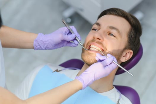 Periodontal Services. Closeup Shot Of Smiling Man Getting Treatment In Stomatologic Clinic, Dentist Doctor In Gloves Using Sterile Dental Tools For Examining Teeth Of Male Patient photo