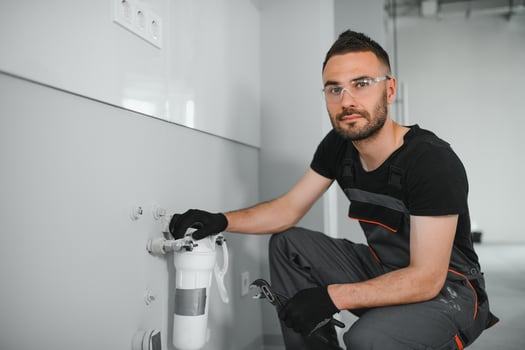 Young man in workwear using pliers while installing water filtration system photo