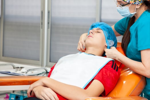 Young male patient being prepared for a skin lesion removal procedure. Dermatologist carrying out a removal of benign skin lesion on the face of a young male patient. photo