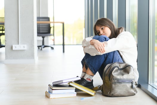 Upset teen girl sit on floor sadly look out window worried about teenage problem at school photo