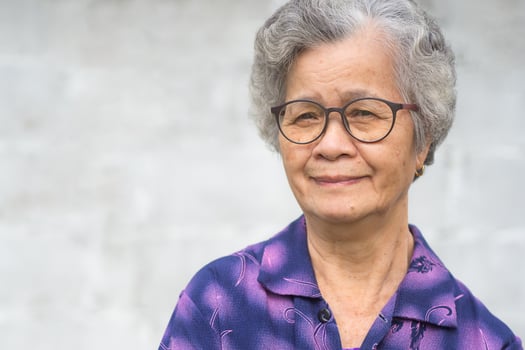 Cheerful senior woman with short gray hair wearing glasses, smiling and looking at the camera standing by white wall. Space for text. Concept of aged people and healthcare photo