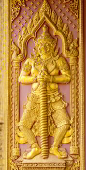 Intricate Golden Carved Guardian Statue on Temple Door in Thailand photo