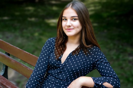Emotional girl teenager with long hair hairstyle braids in a green shirt sits on a bench in the park. photo