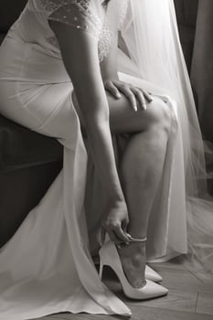 A woman in a wedding dress sits on a couch, putting on her shoes. Concept of elegance and sophistication, as the woman is dressed in a formal gown and is taking care to put on her shoes properly photo