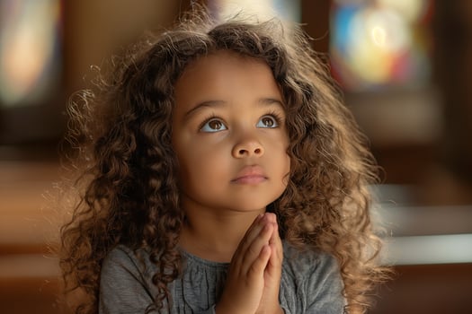 A little girl with curly hair, wearing gray and praying in the church with hands clasped together photo