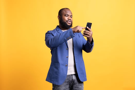 BIPOC man texting best friend using smartphone, reading messages. Relaxed african american person having fun while chatting with mate on mobile phone, isolated over studio background photo