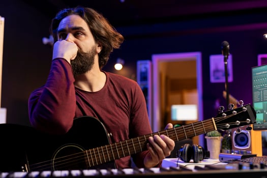 Stressed artist staying up all night playing guitar and recording tunes, contemplating about new lyrics for a song. Exhausted frustrated songwriter thinks about acoustic instrument accords. photo