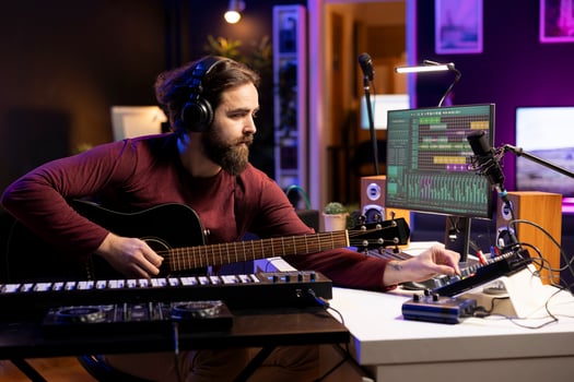 Singer creating tunes on guitar and adding sound effects in post production, uses mixing console and gear. Musician producing and editing audio recordings, playing acoustic instrument. photo